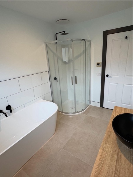 A renovated bathroom with tiled shower and bath by TJC Building