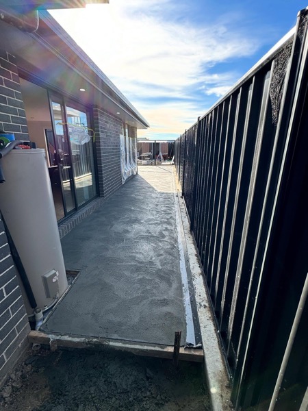 A concrete path poured between a house and fence by TJC Building
