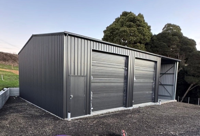 A completed dark grey shed with roller doors and open bay erected by TJC Building