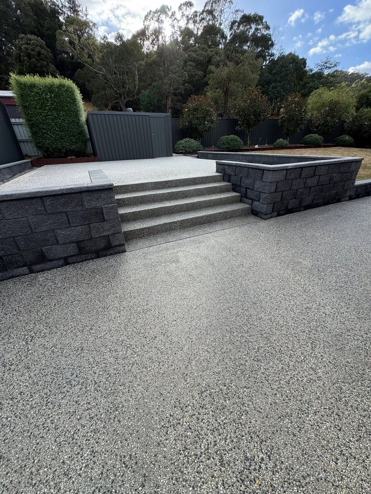 A finished exposed aggregate backyard with steps and block retaining walls by TJC Building